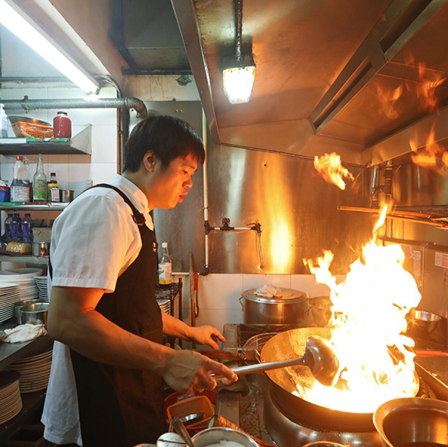 A man in a kitchen cooking in a wok over open flame