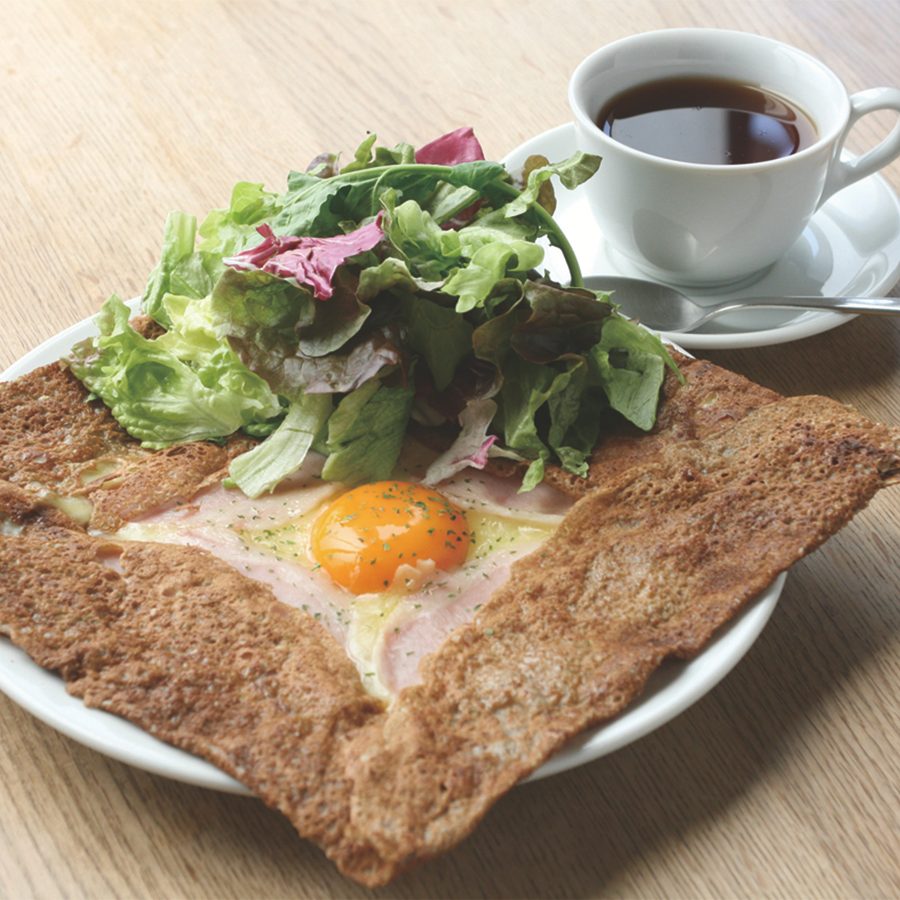 A plate of ham and egg crepe with salad and a cup of black coffee on a wooden table served at B.B.B Potters in Fukuoka, Japan