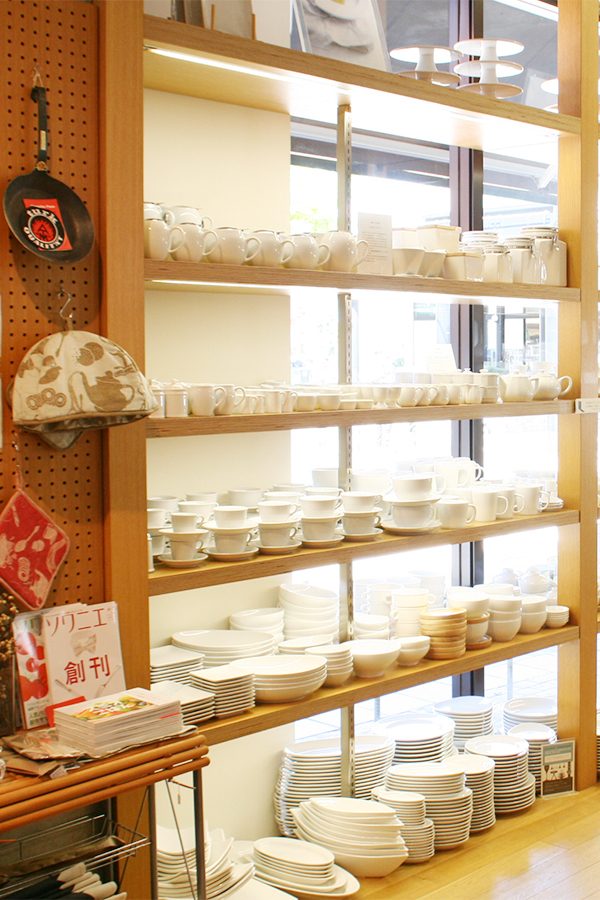 A collection of plain ceramic plates, bowls and cups on shelves next to windows inside B.B.B Potters in Fukuoka, Japan