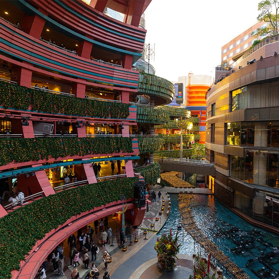 A view inside Canal City Hakata shopping complex in Fukuoka featuring its colourful buildings, green foliage, mall pond and busy shoppers walking around