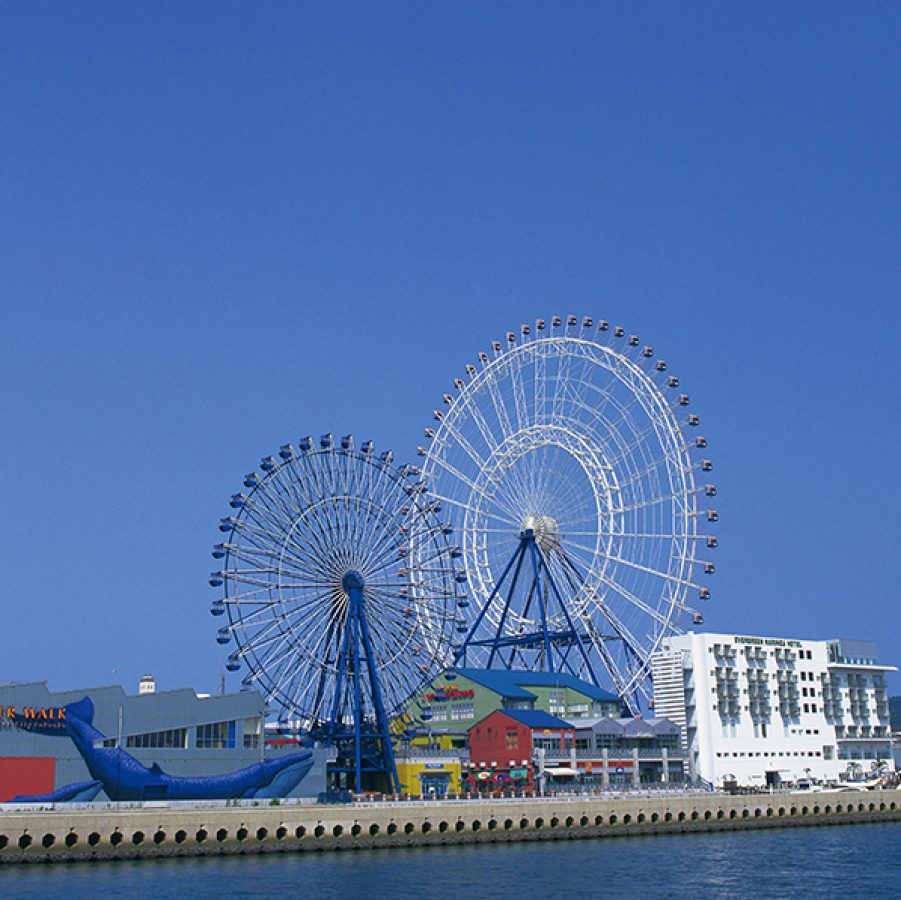 A seaside view of Marinoa City Fukuoka Outlet mall by the pier featuring two ferris wheels outside during daytime 