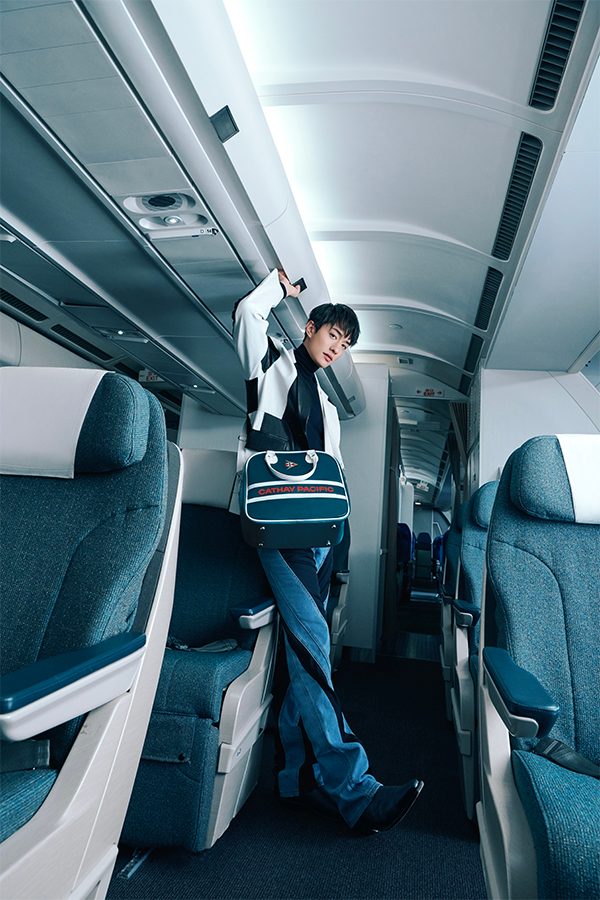 errance Lau wearing a cross-body Cathay Classic bowling bag in dark green in the aisle of an aircraft 