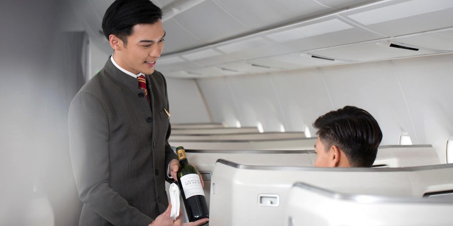 Een cabinepersoneelslid van Cathay Pacific houdt een fles wijn vast voor een passagier in een stoel in Business Class. 