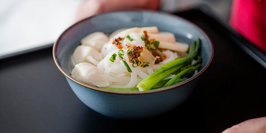 A cabin crew serving a bowl of fish ball noodles on a black tray. 