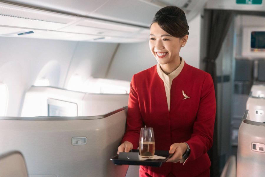  A Cathay Pacific flight attendant, smiling, is holding a tray and on top sits a glass of champagne.