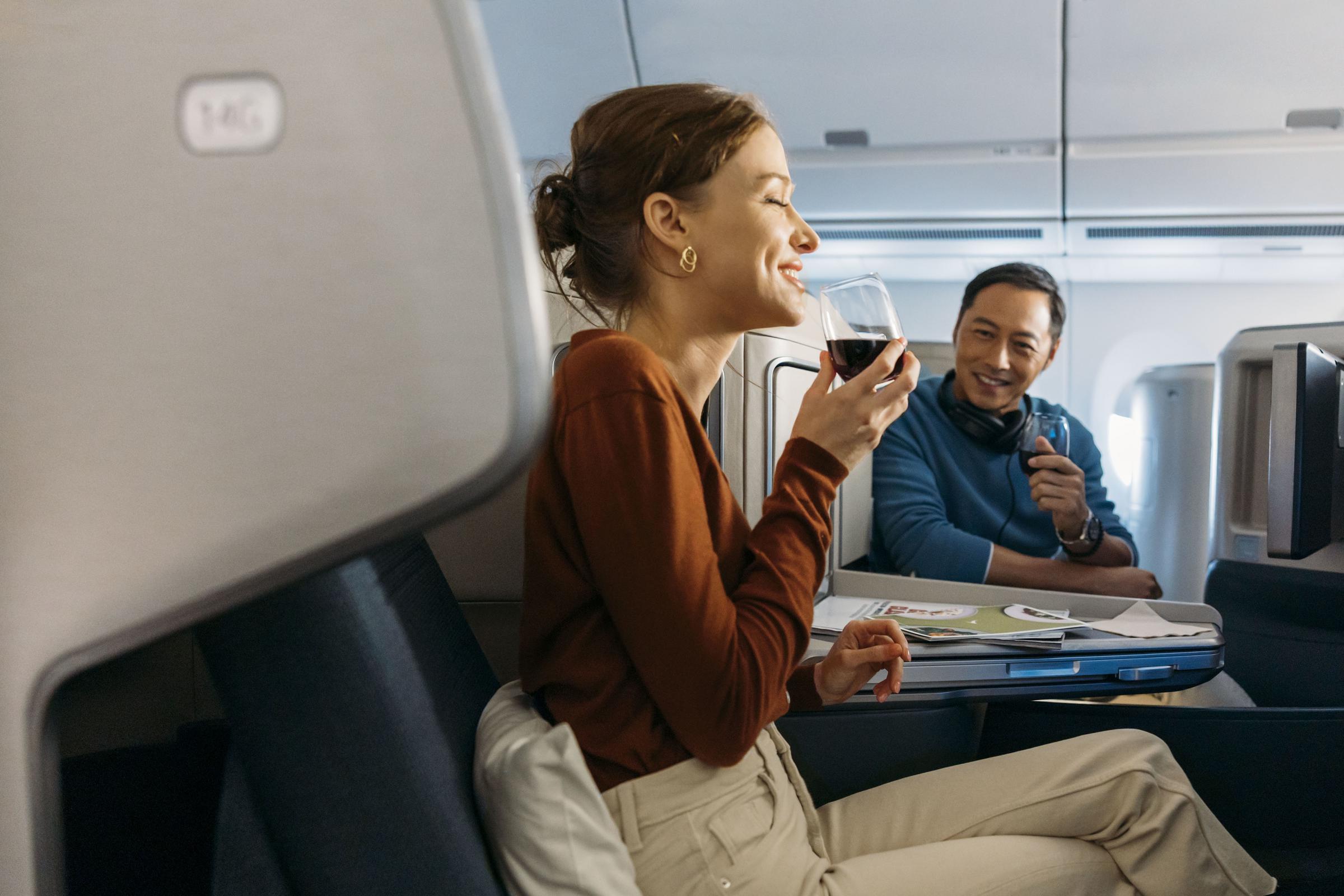 A female and male passenger, both seated in a Cathay Pacific Business cabin, are enjoying a glass of wine on board.