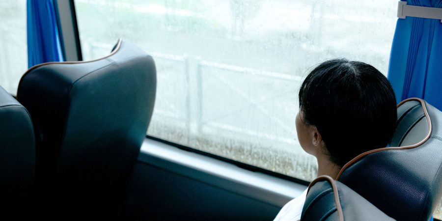  A back view shot of a passenger in a window seat of a shuttle bus. She is looking out to the road through the window.