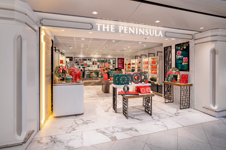 The storefront of The Peninsula Boutique at Hong Kong International Airport. The entrance of the store showcases different products in red and green packaging.