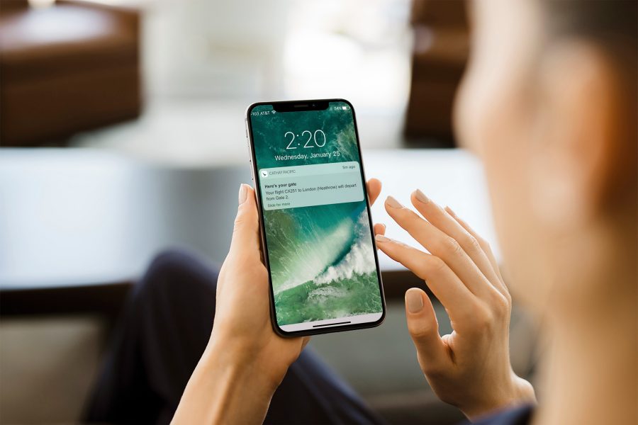 A mobile phone being held up by a person's hands. The phone screen shows a notification from Cathay Pacific about a passenger's boarding gate information. 