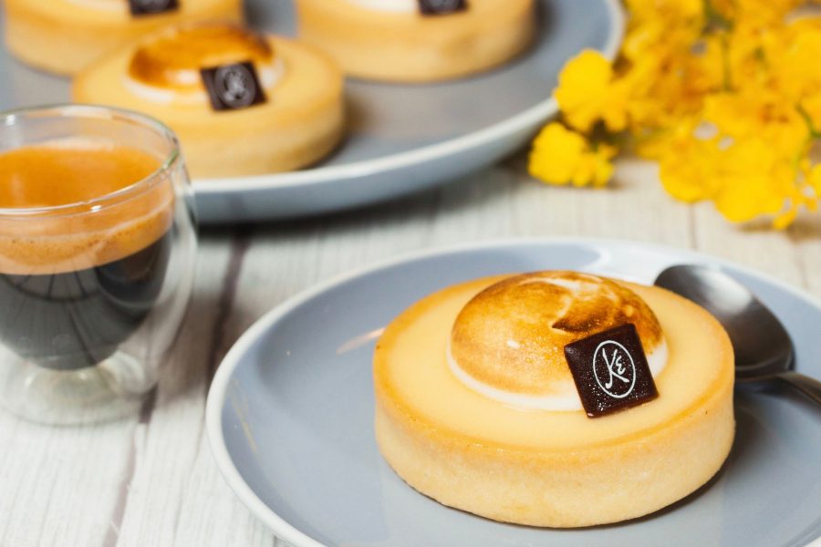 Side shot of a lemon tart and shot of espresso coffee on a light wooden table.