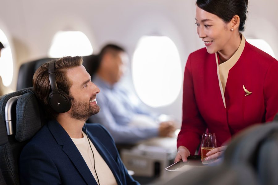 A Cathay Pacific flight attendant serving a drink to a passenger on board. The two are smiling at each other.