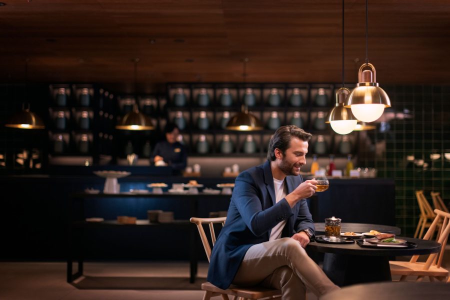 A man enjoying a cup of tea and refreshments in an atmospheric dining area with moody lighting and dark wood furnishing.